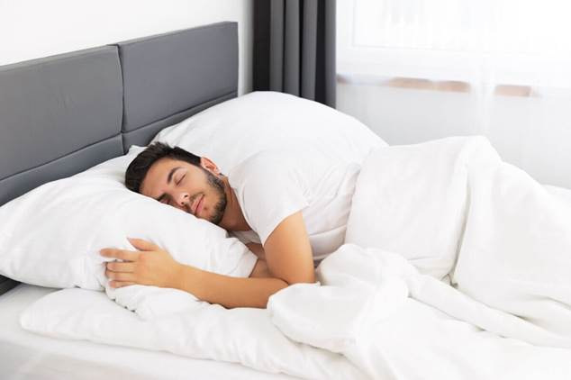 Persona durmiendo plácidamente en un dormitorio luminoso y confortable, lo que ilustra el sueño reparador como pilar del bienestar.