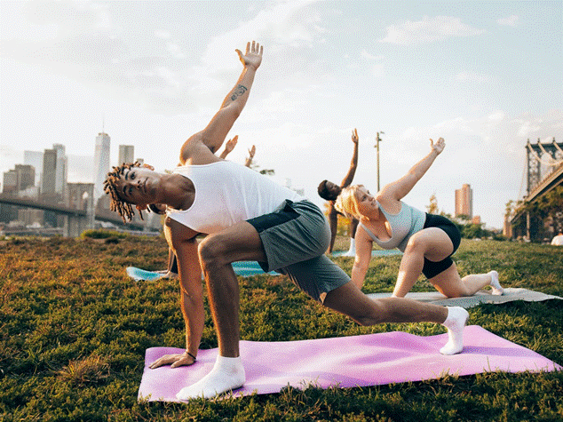 Personas practicando yoga al aire libre en un parque urbano, promoviendo el ejercicio y el bienestar.